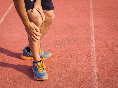膝盖受伤了运动的男子与强壮的运动腿握膝与他的手疼痛后, 在跑步锻炼训练跑步过程中肌肉受伤的运行轨道。保健和体育概念.