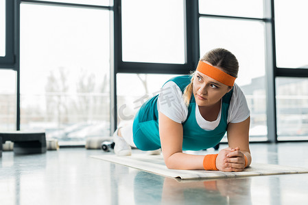 超重女孩在健身房的健身垫上做木板运动