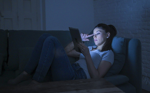 年轻美丽疲惫和无聊的拉丁女人30s 躺在家里的沙发上深夜使用数字设备笔记本电脑 tablet 垫看互联网电影 