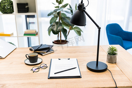 办公室办公场所的咖啡、眼镜、文件和台灯的特写图