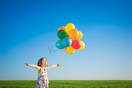 气球绿色摄影照片_快乐的孩子在户外玩色彩艳丽的气球.在蓝天背景下,孩子们在绿色的春田里玩得很开心.健康和积极的生活方式概念