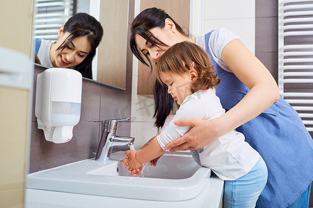 洗手池疏通摄影照片_孩子妈妈在浴室里用水洗手.