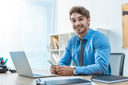 agent摄影照片_cheerful travel agent looking at camera while sitting at workplace