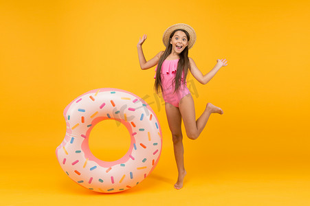 一个有趣的配件。快乐的童年小女孩戴着草帽，穿着泳衣。带着黄色背景微笑的孩子。假日和假期。泳池派对带着橡皮圈的无忧无虑的孩子。夏季海滩活动
