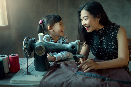 sewing摄影照片_Mother and daughter are happy. To help sew or sew with a sewing machine.
