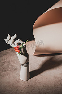 玫瑰花黑色摄影照片_粉红色的玫瑰花在机器人手在石头桌上与纸纸隔离在黑色