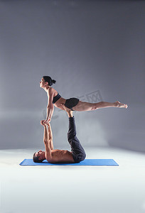 双人瑜伽摄影照片_年轻夫妇一起练习杂技瑜伽工作室在垫子上。杂技。几个瑜伽。双人瑜伽.