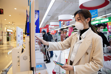 戴口罩细菌摄影照片_戴口罩的青年女人在超市用手机付款