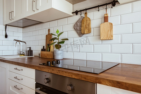 白色砖墙摄影照片_厨房黄铜器皿，厨师配件。用白色瓷砖墙和木桌挂厨房。厨房背景上的绿色植物