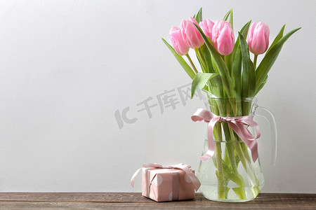 美丽的粉红色郁金香花花束在花瓶和礼品盒在灰色的墙壁背景。文本的位置。春天。假期.
