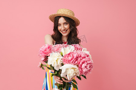 拿着照片摄影照片_快乐快乐微笑的年轻可爱的女人摆出孤立的粉红色墙壁背景拿着花.