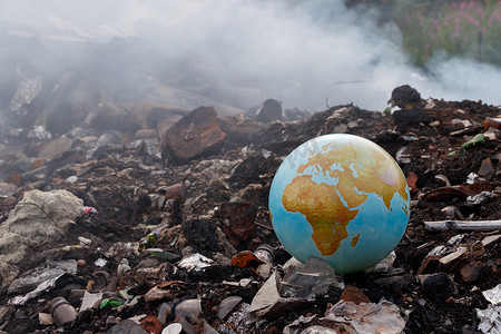 扔摄影照片_概念对垃圾焚烧环境的问题。焚烧厂对环境有害。地球被扔进垃圾桶。垃圾焚烧烟雾来了有毒二恶英.