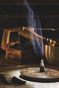 风格摄影照片_在藏人碗和一些蜡烛旁边点上了香筒。蓝色的烟冥想、瑜伽、平静、治疗和宗教观念。黑暗的风格垂直方向