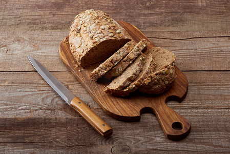 新鲜烤切面包与种子在木切碎板附近的刀在桌子上