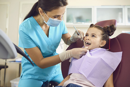 在牙科诊所，一名带着面具和手套的儿科牙医的小女孩为儿童牙齿护理服务.