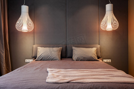 室内设计新颖的现代居室，舒适的床上点着灯光灯，床罩上有枕头，背靠着柔软的头枕