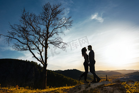 情人摄影照片_一对恋爱中的情侣的剪影。在日落时拥抱的男人和女孩。一对夫妇的旅行。自然界中的情人。看日落的男人和女人。日落时的情人。在山里旅行。蜜月之旅