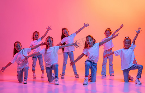 dance摄影照片_Hip-hop dance, street style. Group of children, school age girls in casual style clothes dancing in choreography class isolated on pink background in yellow neon light. Concept of music, fashion, art