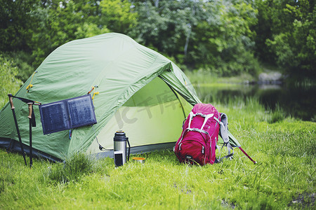 河岸摄影照片_在河岸上露营。太阳能电池板悬挂在帐篷上.