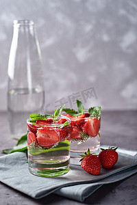 饮料夏季摄影照片_将草莓和薄荷倒入晶莹的玻璃杯中倒入水中,复制空间.寒冷的夏季饮料。矿泉水