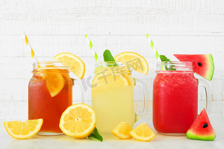 各种夏季饮料在石匠罐玻璃杯与水果与白色木材背景。冰茶、柠檬水和西瓜汁.