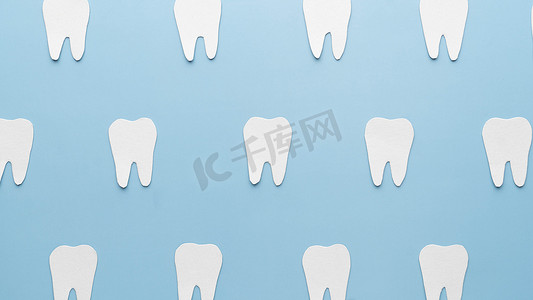 用浅蓝色背景的纸制成的白色牙齿形状的顶部视图。牙的概念。最低限度.