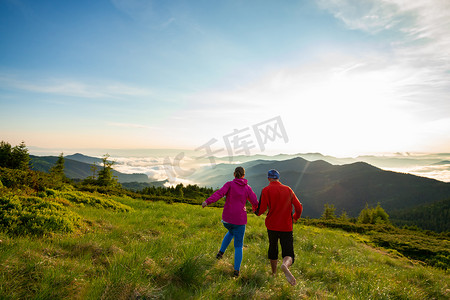 奔跑背摄影照片_快乐的情侣正在奔跑, 并有乐趣, 高兴, 从山上的可怕的景色在日落。史诗般的旅行在山上。广角、后视、背光源.