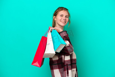 Young English woman isolated on blue background holding shopping bags and smiling