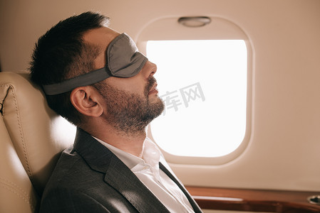 坐在私人飞机上的戴着睡眠面具的商人的侧视图 