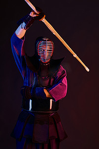 戴钢盔摄影照片_近距离射击，剑道战士身穿盔甲，传统和服，钢盔练武，剑鞘竹剑，黑色背景.
