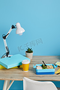 蓝底摄影照片_蓝底木制桌子上有灯、文件夹和美味午餐的工作场所