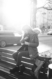 年轻漂亮的女孩坐在长凳上。一只手挂着她的围巾