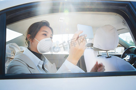 戴口罩的年轻女人坐在汽车里看手机