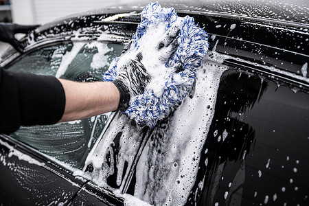 小心摄影照片_洗车厂或汽车维修车间的员工小心地清洗一辆黑色汽车.