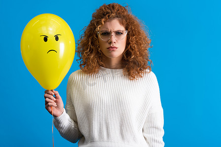 aggressive摄影照片_aggressive woman holding yellow balloon with angry face, isolated on blue