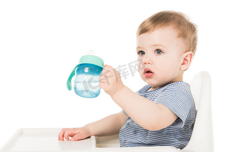 可爱的小男孩抱着婴儿杯水和坐在高脚孤立的白色背景 