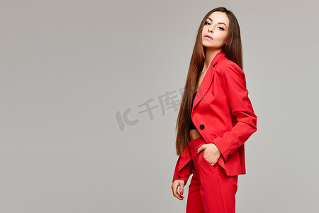 穿着时髦红色西服的模特女孩的侧视图，灰色背景与复印空间相隔离