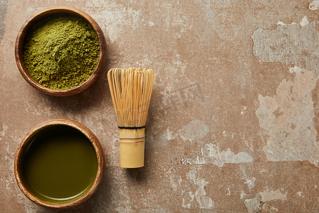 木碗中火柴茶和绿色粉末的顶视图，在老化表面用竹须