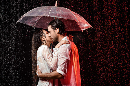 黑色背景下雨中的白色衬衫与雨伞的浪漫情侣的侧面视图