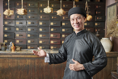 快乐的亚洲男人做出欢迎的姿态，并邀请顾客来中国传统药店