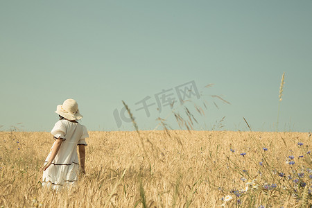 Summer dreams. Girl walking in a field of wheat with blue sky re