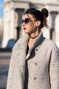 意大利米兰大街上，迷人的年轻女子身穿灰色外套，一头乌黑的长发，戴着太阳镜，站在室外。美丽的高加索模型肖像。步法时尚