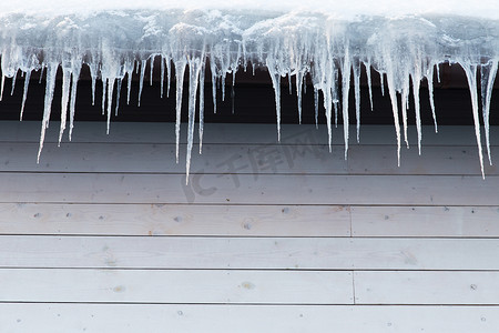 房子上盖着冰柱，特写。冰钟乳石挂在屋顶上，复制空间。屋顶保温差导致冰柱的形成.解冻，冬季天气概念