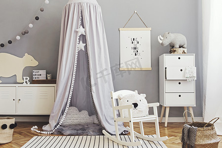 时尚的斯堪的纳维亚新生儿房，有仿制海报、白色设计家具、天然玩具、挂有星星的灰色顶篷、枕头、配饰和泰迪熊。可爱的儿童内饰装饰. 
