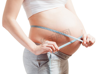 一个怀孕的年轻女子正在用柔韧的身体测量她的大肚子