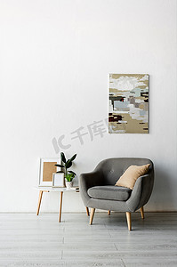 现代客厅里，茶几旁边的灰色扶手椅，墙上挂着画框和绿色的植物 