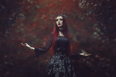 女巫动图摄影照片_一个美丽的女人, 面色苍白, 长着红色的头发, 穿着黑色的连衣裙, 穿着黑色的 crownk。女孩女巫与吸血鬼的爪子和红唇。哥特式的样子。万圣节套装.