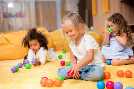 可爱的多文化的孩子在地板上玩彩色球在幼儿园