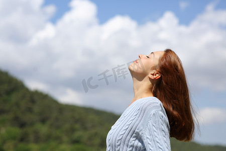 在多云的天空下，一个女人在山上呼吸新鲜空气的轮廓
