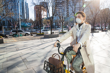 上下班摄影照片_戴口罩的年轻女人骑共享单车